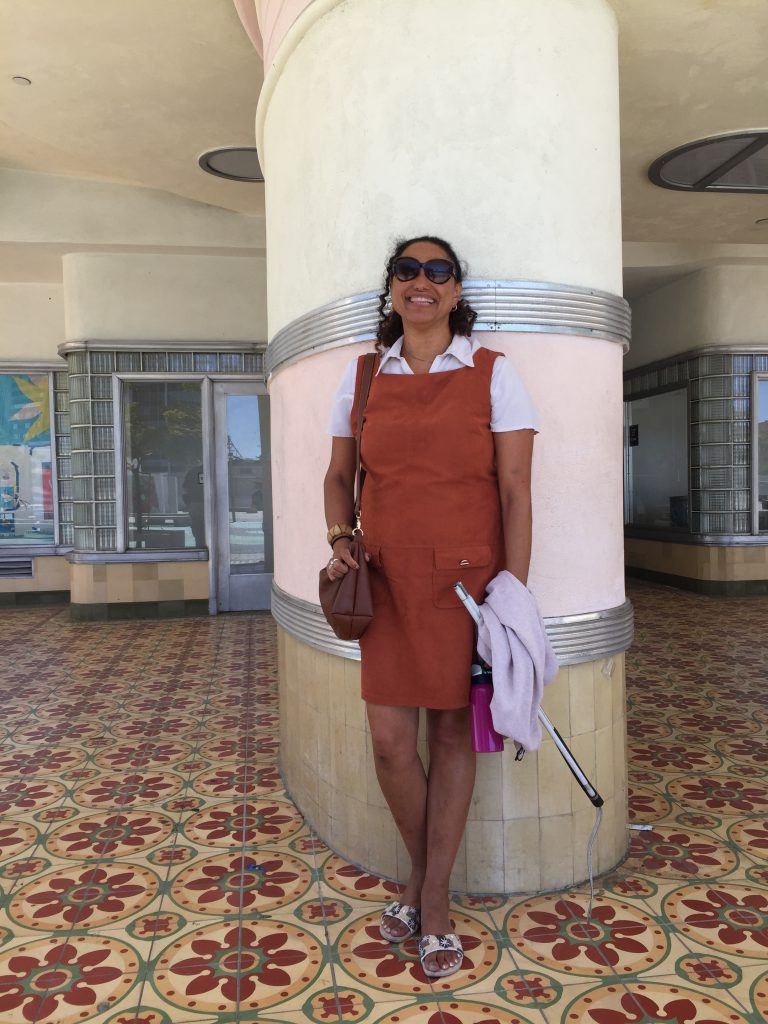 Maria standing in front of a tall column amidst some colourful tiles, on the site of the old Coconut Grove where Lynn first performed