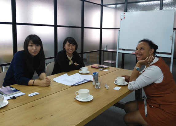 Maria sits at a table in discussion and smiling with Mariko Mori and Mei Harada at The Nippon Foundation.