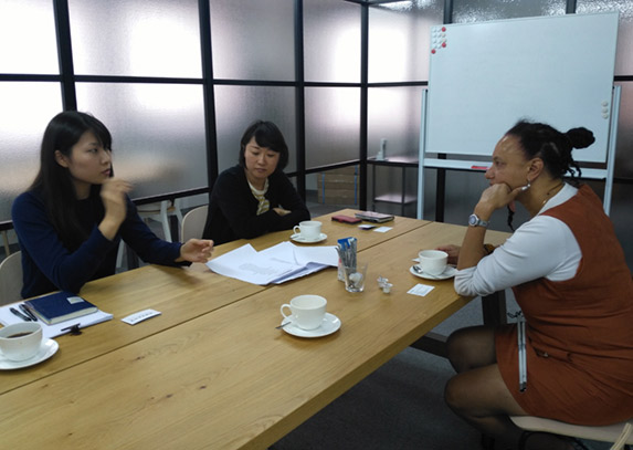 Maria sits at a table in discussion and smiling with Mariko Mori and Mei Harada at The Nippon Foundation.