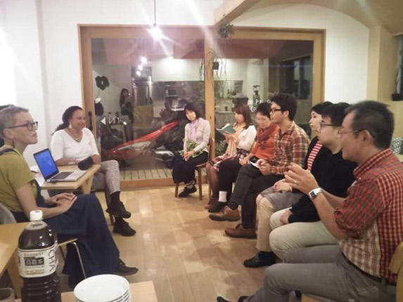 Maria sits at a table talking to the group and is gathered with them for a group photo