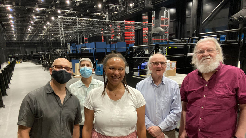 Looking down the length of the vast interior space with the huge platform in the T section at the end. All of the research platforms appear in a long line, with some of the floor to ceiling storage racking  behind them. In the fore-ground from left to right is Nic S,Crin , Maria Nick T and Terry, all white apart from Maria.