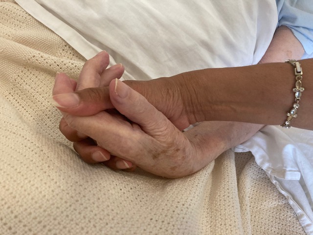 Maria’s hand with brown skin  tone, has an antique bracelet showing, holding older  white woman’s hand 