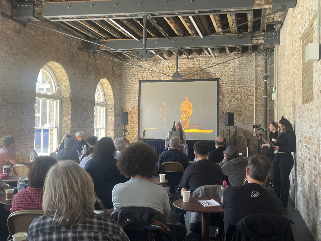 Maria presents in front of a room of delegates.