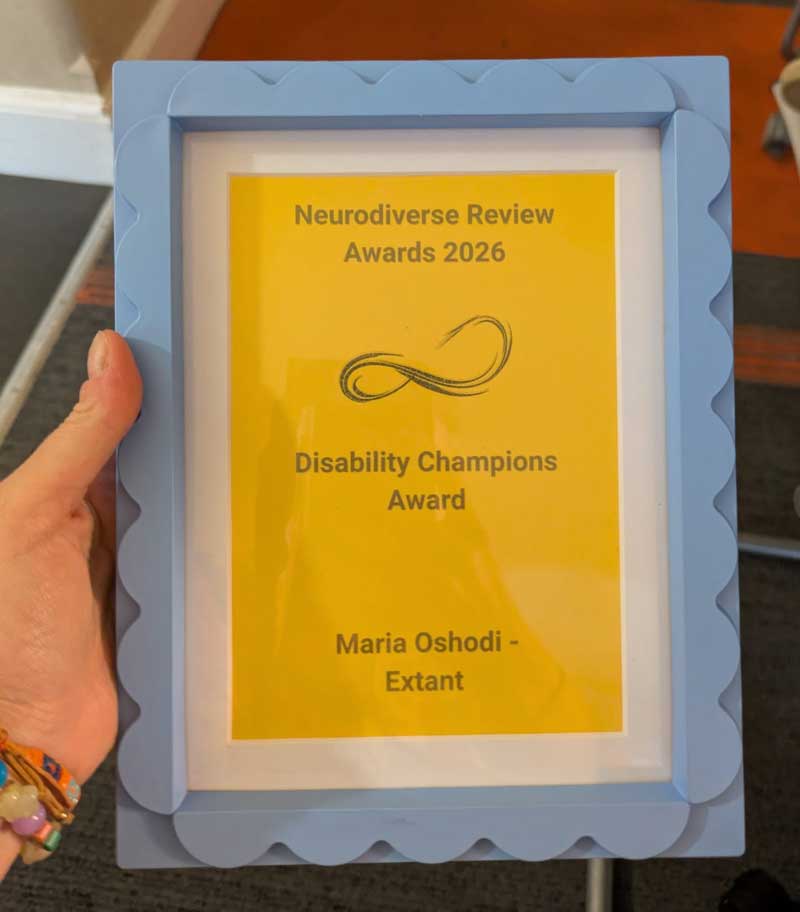 A hand holds the Disability Champions framed certificate. It is a light blue photo frame with scalloped edges. Black writing on a yellow background reads ‘Neurodiverse Review Awards 2026 – Disability Champions Award – Maria Oshodi, Extant’